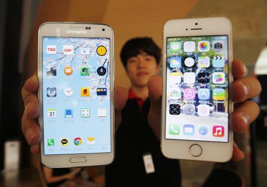 A sales assistant holding Samsung Electronics' Galaxy 5 smartphone (L) and Apple Inc's iPhone 5 smartphone (R) poses for photographs at a store in Seoul July 16, 2014. CREDIT: REUTERS/KIM HONG-JI